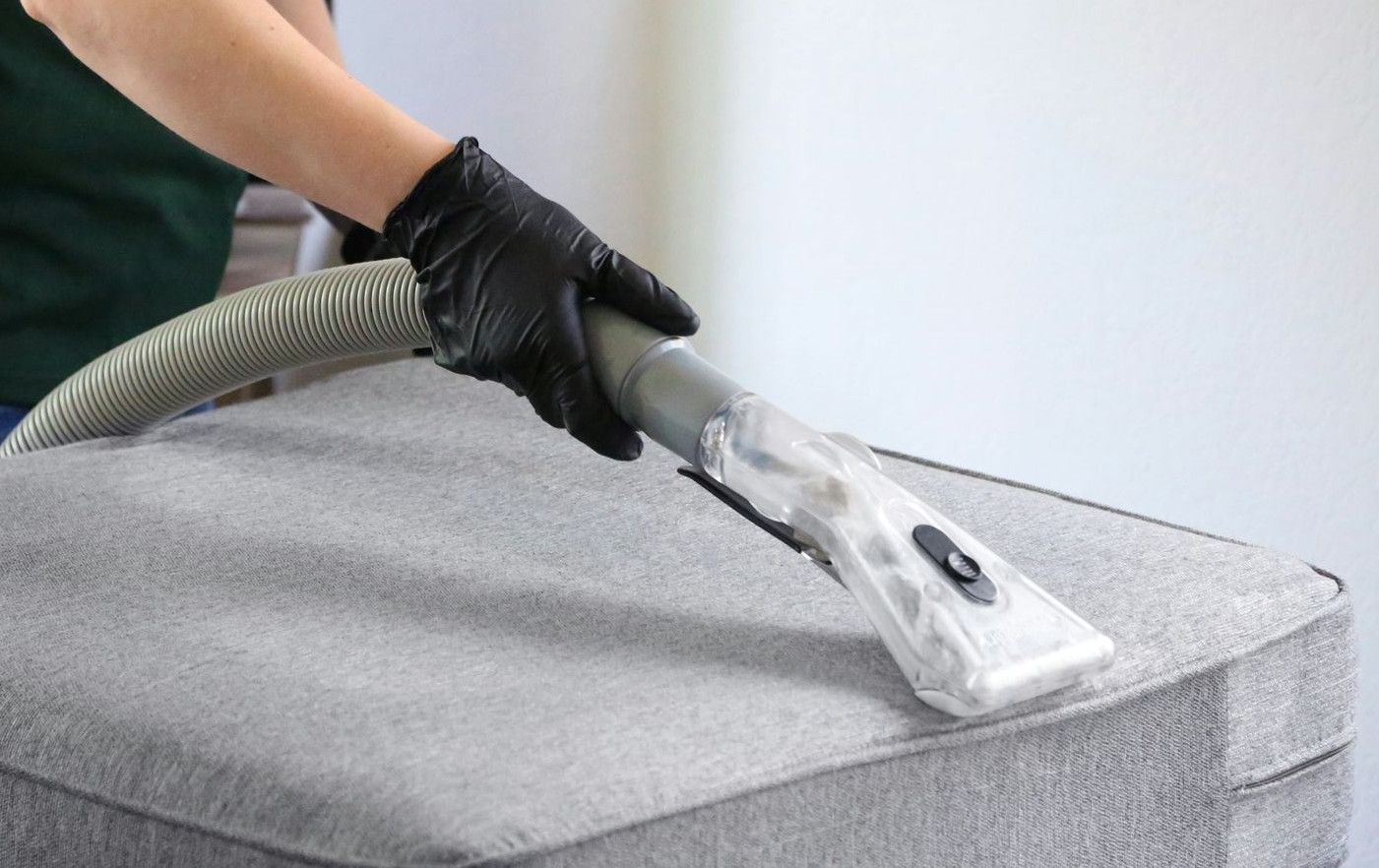 a woman in a green shirt and black gloves vacuuming a gray ottoman